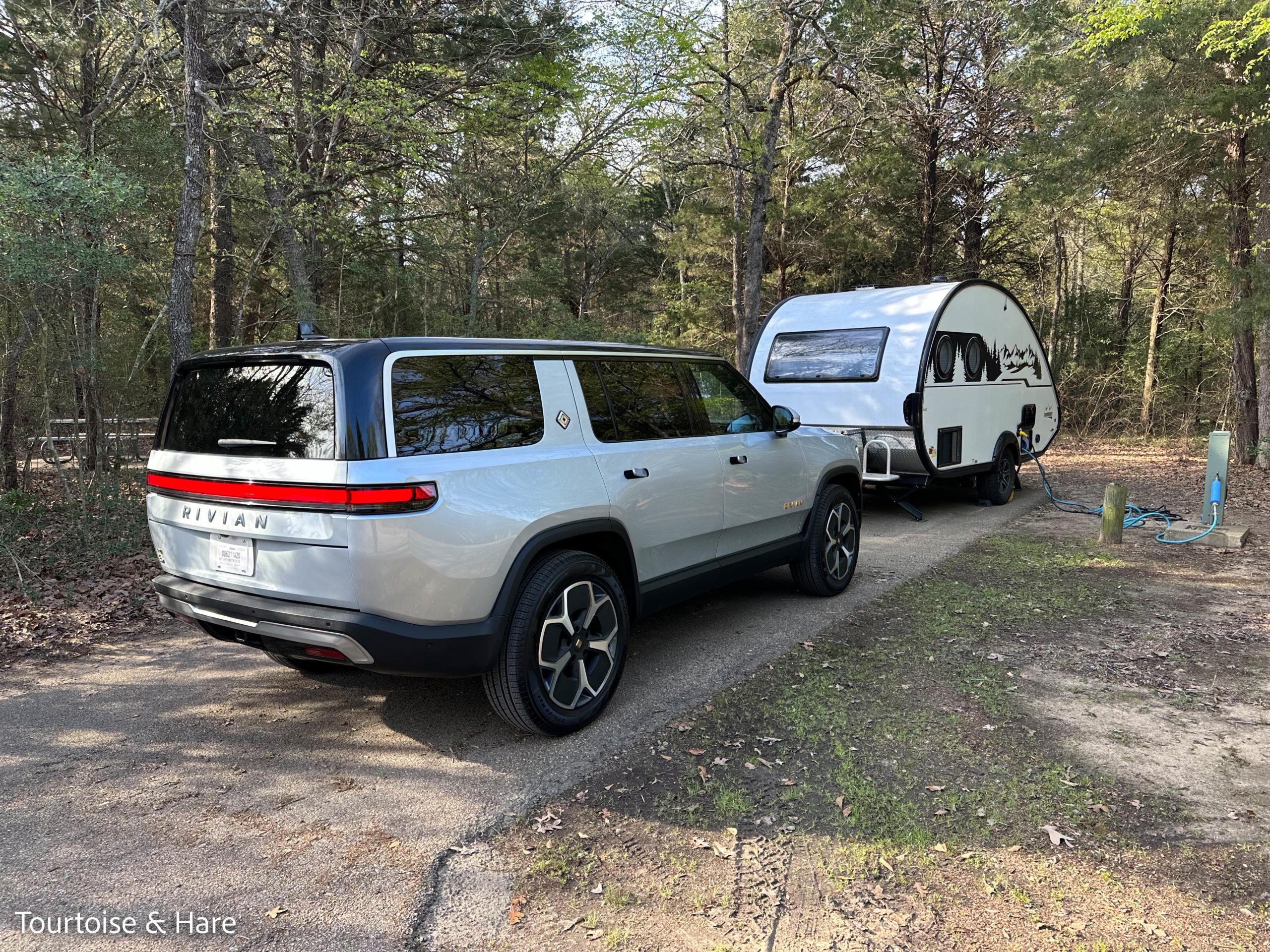 A silver Rivian R1S SUV and a white Tab 400 trailer parked at a campsite