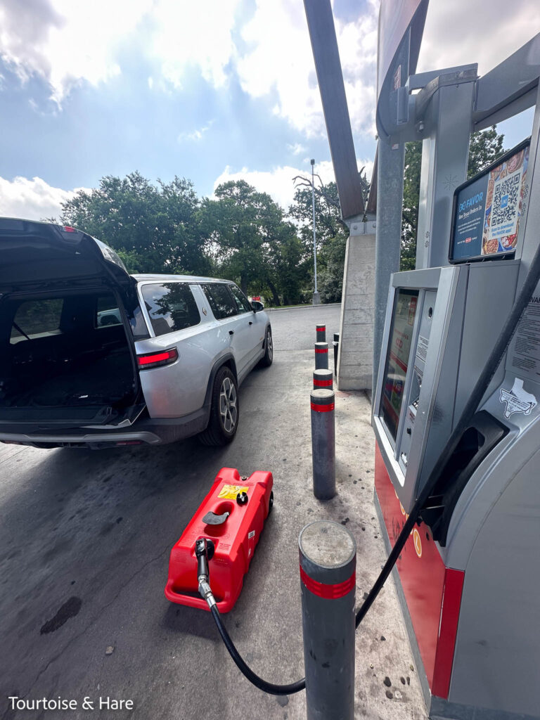 The red gas tank being filled on the ground at a gas pump, with the Rivian's back opened up to put the gas tank in.